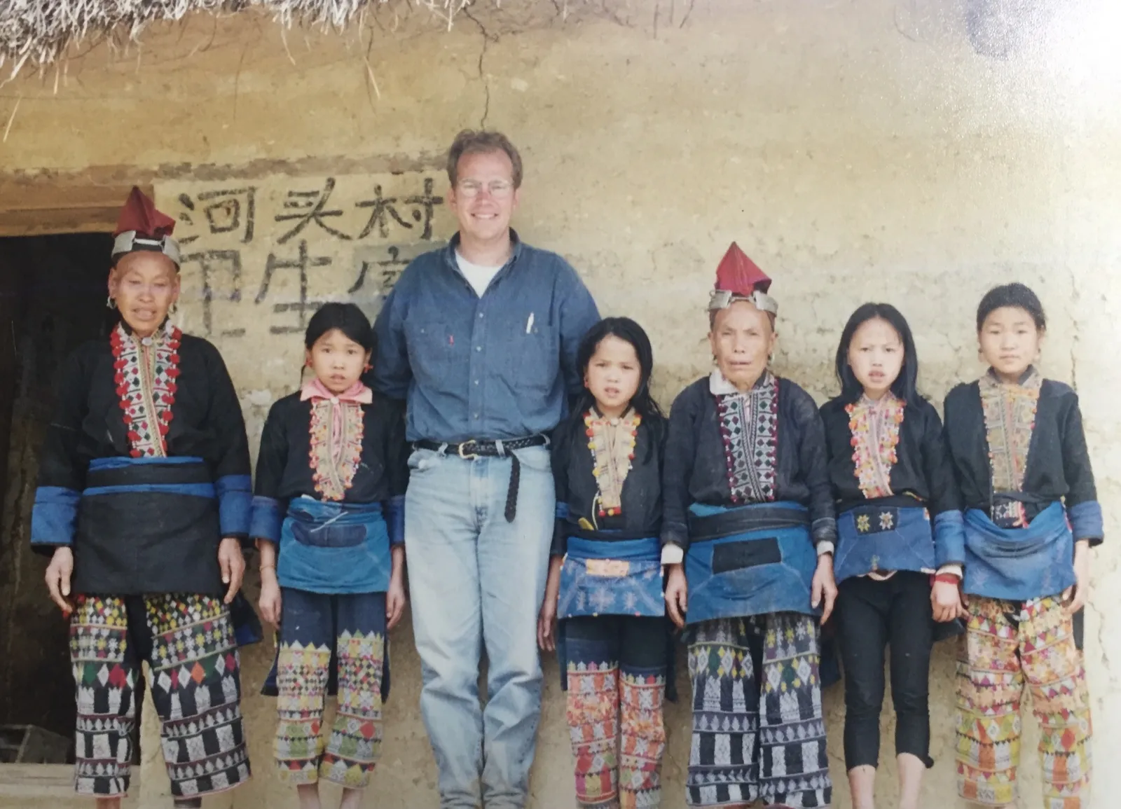 Dr. Briggs standing with women and girls in traditional dress in front of a village wall
